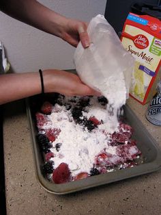 someone is spreading icing on top of a cake in a pan with strawberries and blueberries