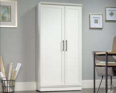 a white armoire sitting next to a desk and chair in a room with gray walls