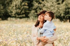 a woman holding a child in her arms while standing in a field full of flowers