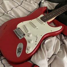 a red electric guitar laying on top of a bed