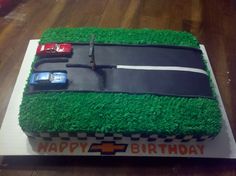 a birthday cake made to look like a race track with cars on it and grass