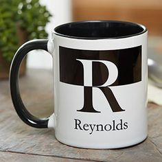 a black and white coffee mug sitting on top of a table next to a potted plant