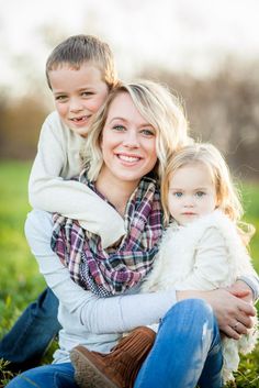 a woman holding a child in her arms while sitting on top of a grass covered field