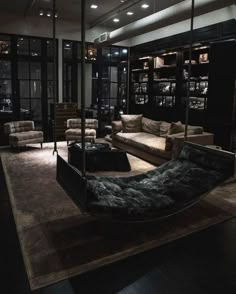 a living room filled with lots of furniture and bookshelves next to windows at night