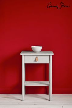 a white bowl sitting on top of a wooden table next to a red painted wall