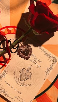 a red rose sitting on top of a piece of paper next to a heart shaped brooch