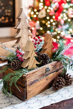 a wooden box filled with pine cones and christmas trees in front of a christmas tree