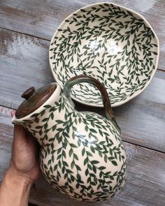 two handmade pottery bowls with leaves painted on them, one is holding a teapot and the other has a saucer