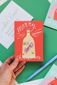 a hand holding up a christmas card on top of some other cards and pencils