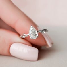 a woman's hand holding a ring with a white diamond on it and a pink manicure