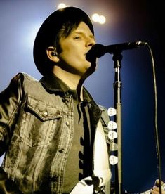 a man with a guitar in front of a microphone and some lights on the stage