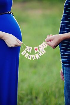 a pregnant woman holding her husband's hand while he holds the word i love you