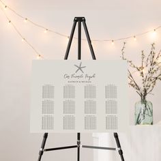 an easel with a seating chart on it in front of a string of lights