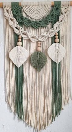 a green and white wall hanging with tassels, beads and shells on it