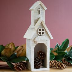 a small white church with a cross on the top and two pine cones in front