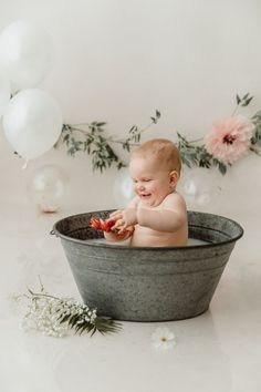 a baby sitting in a tub with flowers and balloons