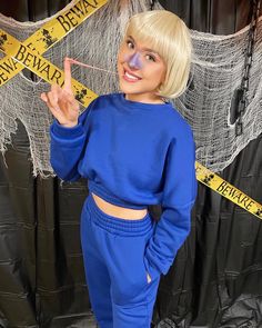 a woman with blonde hair and blue sweatsuit posing in front of a black backdrop