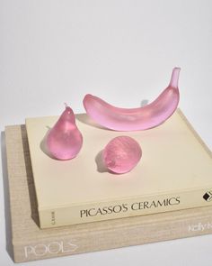 a pink object sitting on top of a book next to a peeled banana and two pieces of fruit