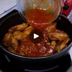 someone pouring sauce into a pot full of chicken wings on top of a stovetop