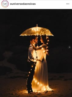 a bride and groom standing under an umbrella on the beach at night with fairy lights