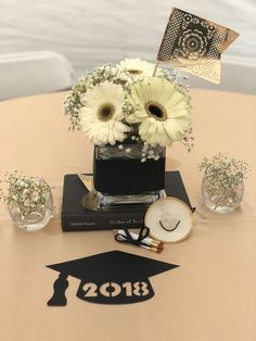 a graduation centerpiece with white flowers in a square vase on top of a table