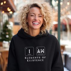 a smiling woman wearing a black hoodie with the words i am elements of experience printed on it