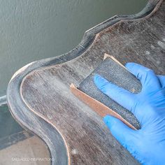 a person wearing blue gloves and holding a sponge on top of a wooden guitar body