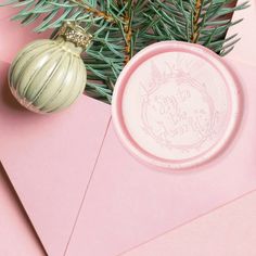 a pink envelope with a christmas ornament and pine tree branch on the top