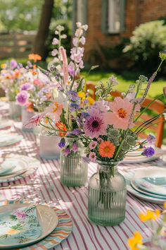 a table set with plates and vases filled with flowers on top of a checkered table cloth