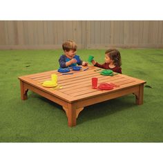 two children playing with toys on a wooden coffee table in the grass, while another child watches