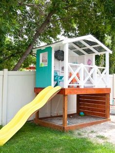 a small play house with a slide in the grass next to a white picket fence