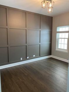 an empty room with wood flooring and gray paneling on the walls, along with two windows