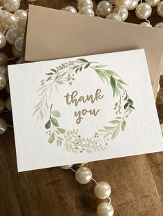 thank you card with watercolor leaves and pearls on the table next to it is an envelope that says, thank you