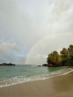 a rainbow in the sky over a beach with waves crashing on it and trees lining the shore