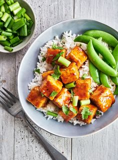 a white plate topped with tofu and rice next to a bowl of green beans