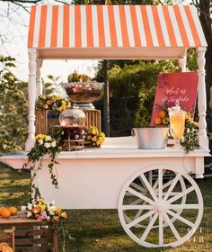 an orange and white striped awning on top of a cart with flowers, lemons and drinks