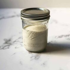 a glass jar filled with white liquid sitting on top of a marble counter next to a spoon