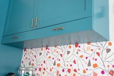 a kitchen with blue cabinets and colorful wallpaper