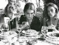 three women sitting at a table with plates and wine glasses in front of their faces