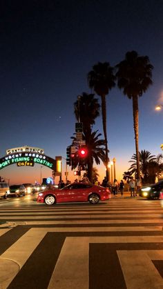 a red car driving down a street next to tall palm trees and a neon sign