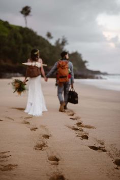 a man and woman walking on the beach holding hands with footprints in the sand as they walk towards the water