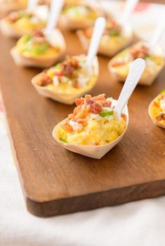 small cups filled with food sitting on top of a wooden cutting board next to utensils