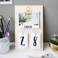 a desk with a calendar, pen and pencils on it next to a potted plant