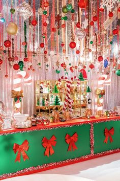 a green and red table topped with lots of christmas decorations next to a wall covered in hanging ornaments