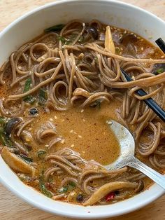 a white bowl filled with noodles and soup on top of a wooden table next to a spoon