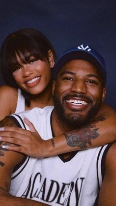 a man and woman hugging each other with tattoos on their arms in front of a dark background