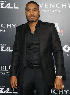 a man in a black suit standing on a red carpet with his hands in his pockets