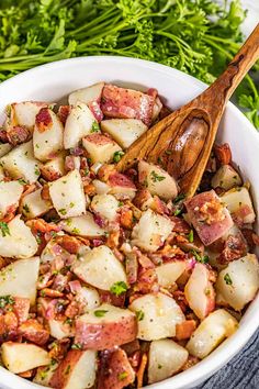 a white bowl filled with potatoes, bacon and parsley next to some fresh herbs