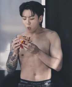 a shirtless man holding a hot dog in his right hand and looking at it