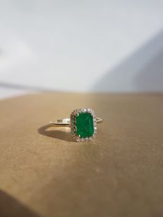 an emerald and diamond ring sitting on top of a table